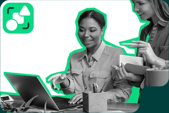 Una mujer sonriente trabajando en una computadora portátil mientras una colega le pasa una tableta