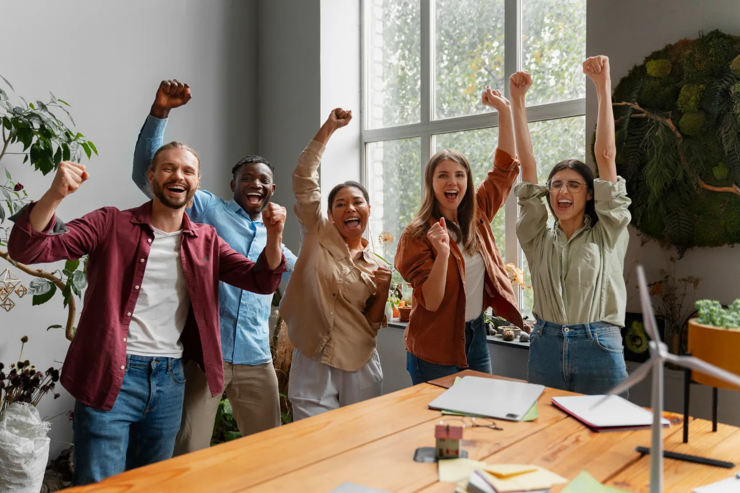 Un equipo celebra con los brazos en alto alrededor de una mesa de trabajo